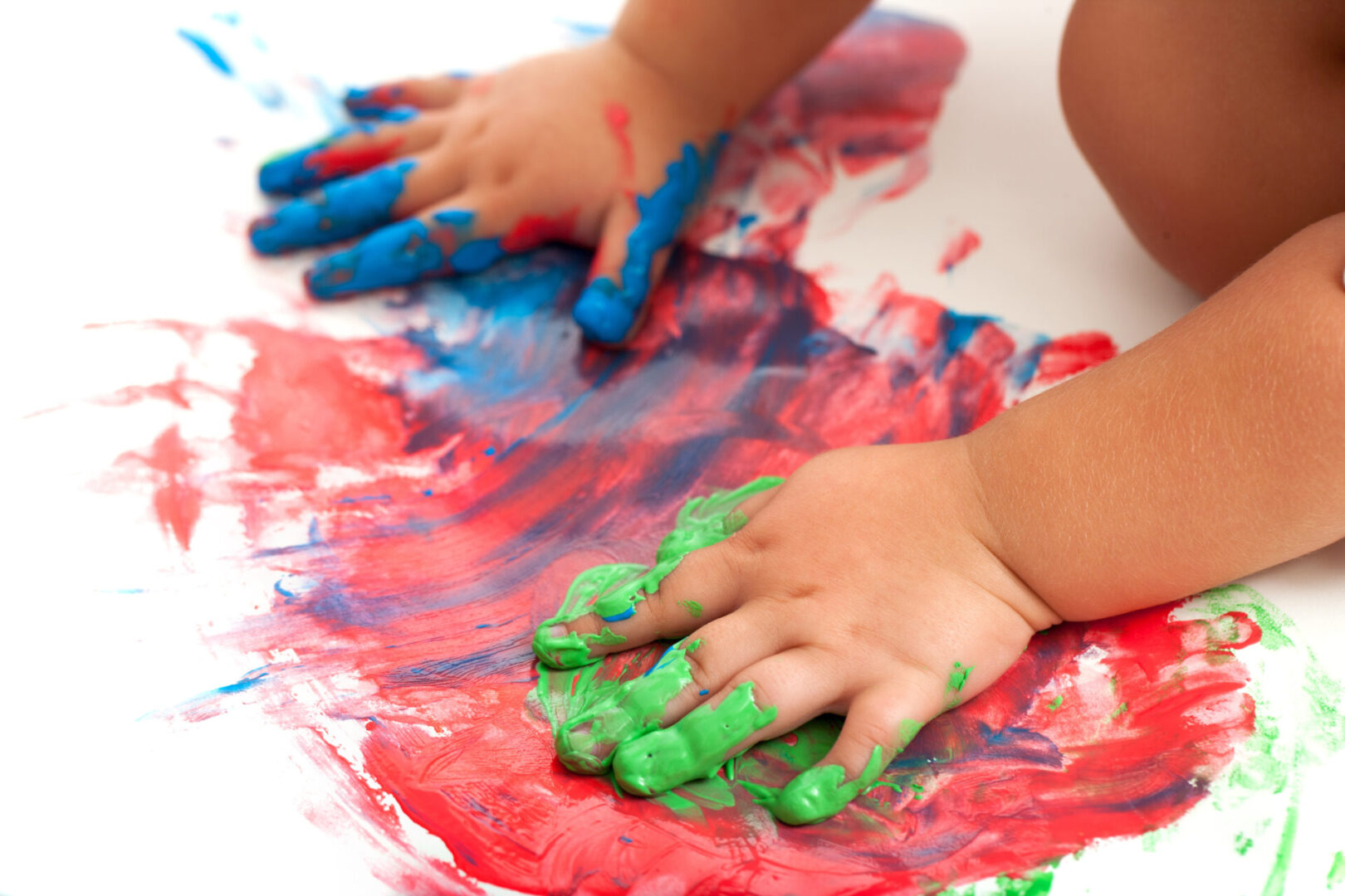 Close up of babies hands painting colorful mosaic. Isolated on white.