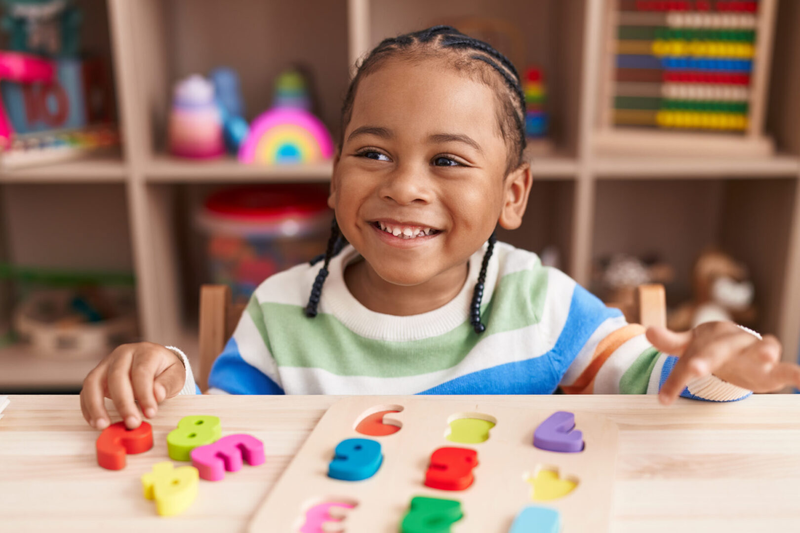 African american boy playing with maths puzzle game sitting on table at kindergarten